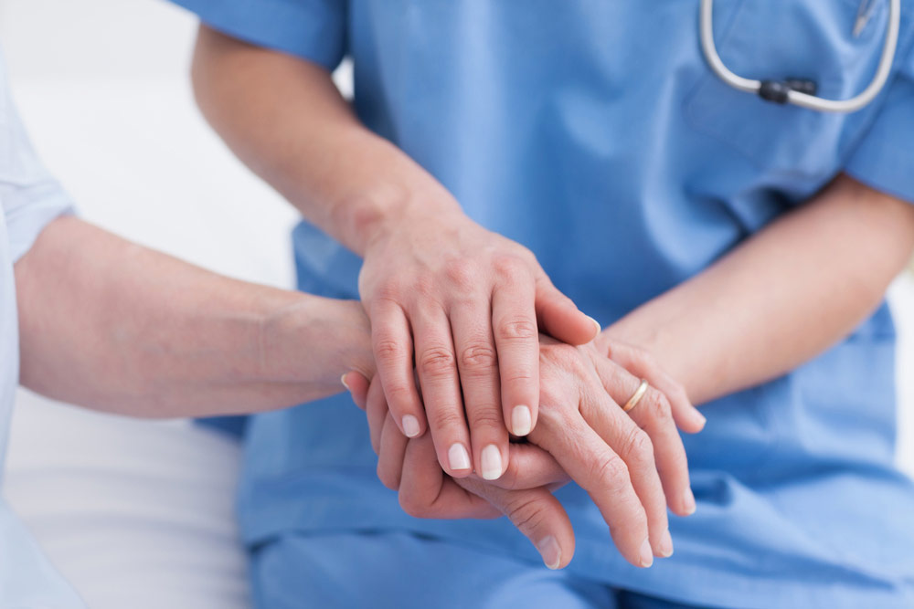 患者様の手を優しく包む看護師の手
